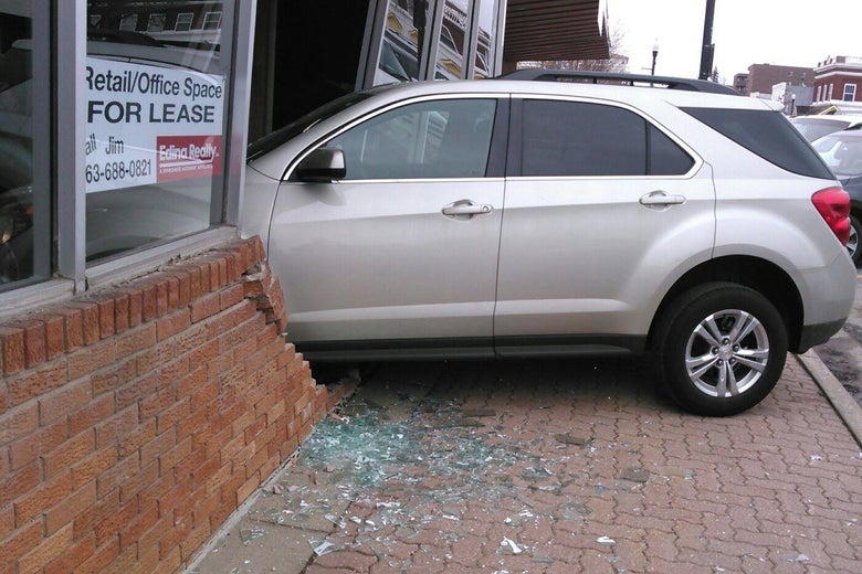 A car surrounded by shattered glass that has crashed through the front of a building.